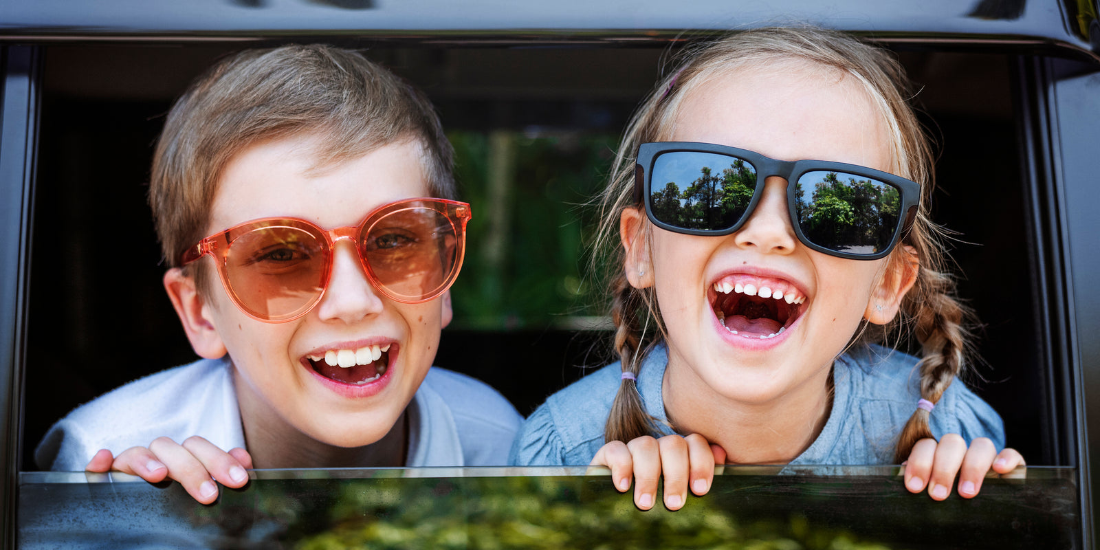 cute happy kids wearing sunglasses hanging out of car window