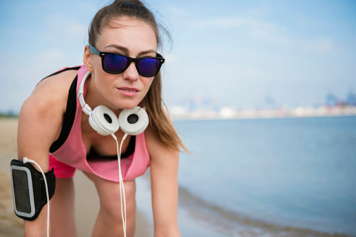 close up-young-fit-person-jogging-by sea wearing sunglasses and headphones