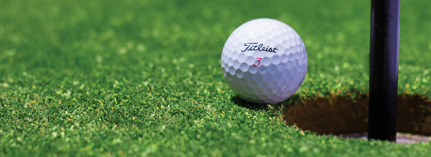 titleist number 3 golf ball on the putting green next to the hole